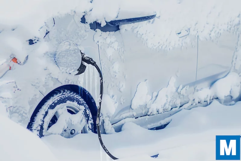 Electric car covered in deep powder snow with charging cable plugged